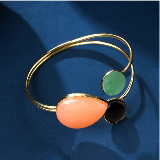 A gold-colored bracelet with black, green, and peach-colored faux stones on a blue background.