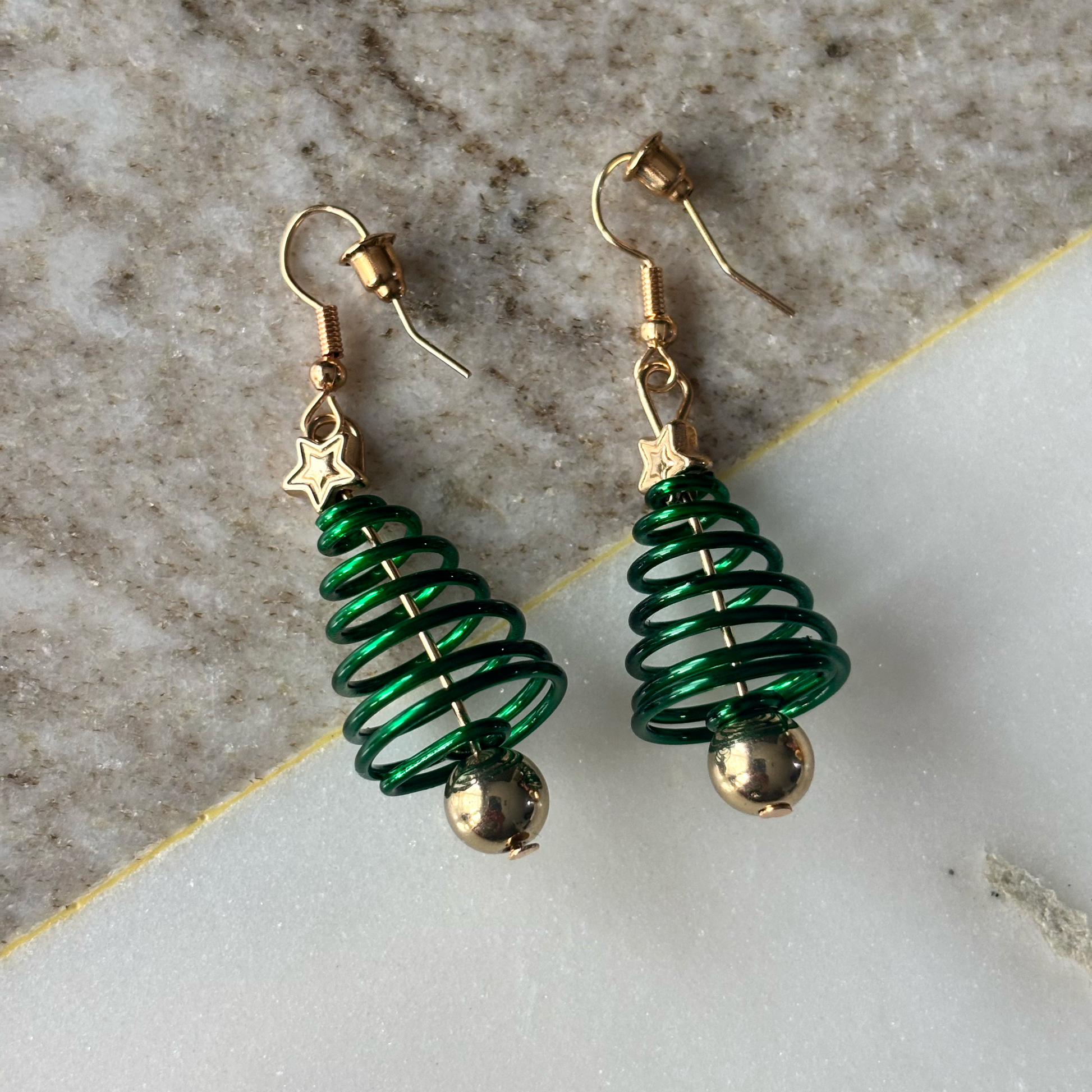 Green spiral earrings with gold accents on a marble surface